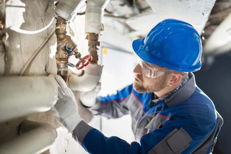 A plumber wearing blue hard hat is inspecting a water pipeline