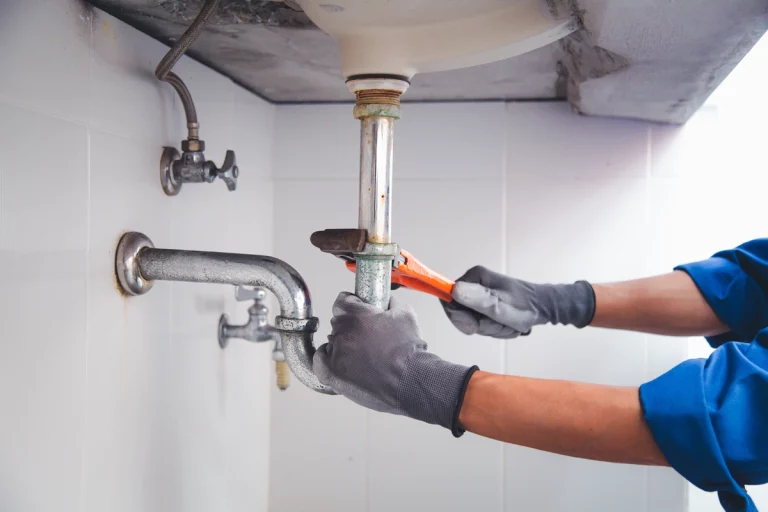 A man wearing gloves is repairing the sink