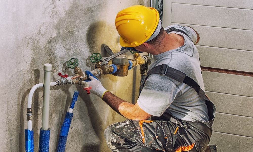 A worker is holding the pipes around while repairing the faucet